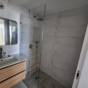 מקלחון זכוכית עם ראש מקלחת עגול על קיר אריחים אפור