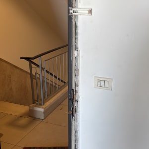 דלת פתוחה עם מסגרת שבורה ומעקה מדרגות ברקע