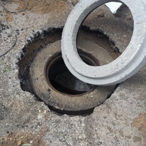 פתח ביוב פתוח עם מכסה בטון מונח בצד