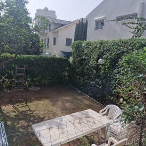 גינה עם שולחן וכיסאות פלסטיק, עצים ושיחים