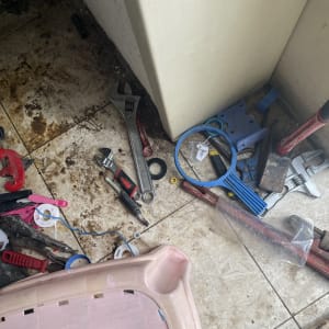 כלי עבודה שונים על רצפה מלוכלכת, כולל מפתח צינורות ומברג.