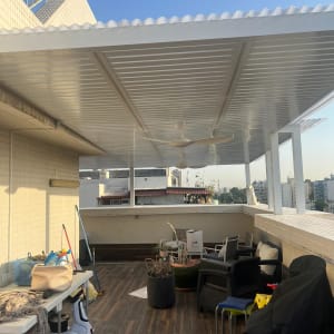 פרגולה מאלומיניום על מרפסת עם ריהוט גן וצמחים