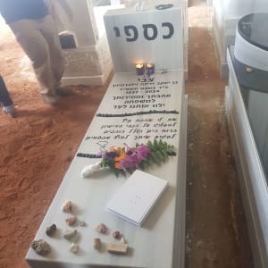 מצבה עם כיתוב בעברית, נרות, פרחים ואבנים