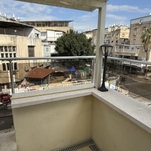 מרפסת עם מעקה זכוכית ונוף לבניינים סמוכים