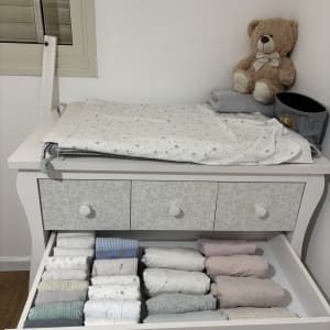 מגירות עם בגדי תינוקות מסודרים ליד דובון צעצוע