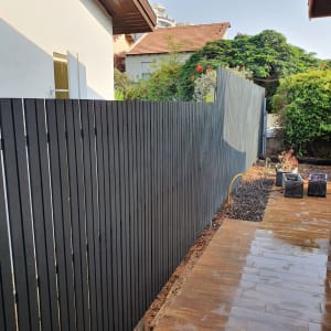 גדר עץ כהה לצד שביל מרוצף רטוב