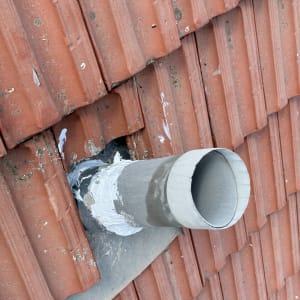 צינור מתכת על גג רעפים אדום עם איטום לבן