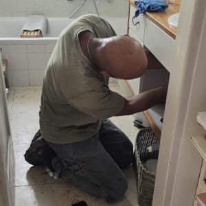 אינסטלטור בעבודה מתחת לכיור בחדר רחצה