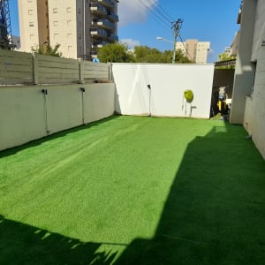 דשא סינתטי בחצר עם צינור השקיה על הקיר