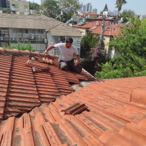 אדם מתקן רעפים על גג רעפים אדום