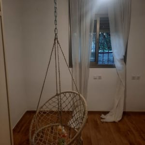 חדר מגורים עם קירות צבועים בלבן, רצפת פרקט וערסל מקרמה תלוי