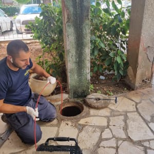 אדם עם כפפות מחזיק כבל ליד פתח ביוב