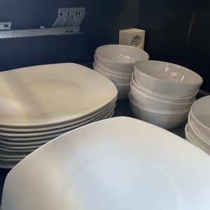 צלחות וקערות לבנות מונחות בארון עם שקע חשמלי ברקע