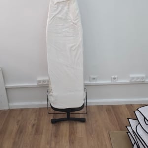 קרש גיהוץ עטוף בניילון עומד על רצפת עץ
