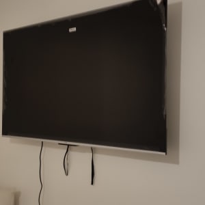 A mounted TV on a wall with visible cables hanging below.