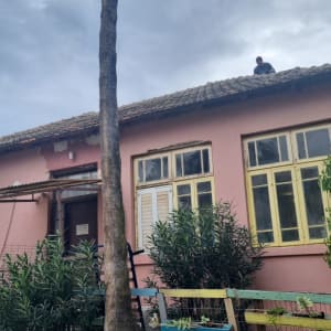 אדם עומד על גג רעפים של בית ורוד.