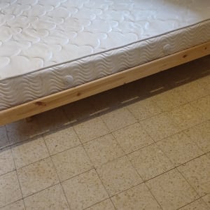 מיטה עם מזרן ובסיס עץ בחדר מרוצף
