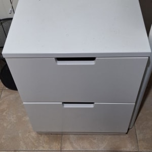 שידה לבנה עם שתי מגירות על רצפה מרוצפת