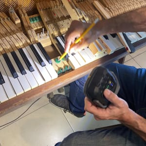 אדם מכוון פסנתר עם עיפרון וכלי מדידה