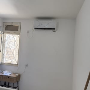 מזגן מותקן על קיר בחדר עם חלון ושולחן קטן