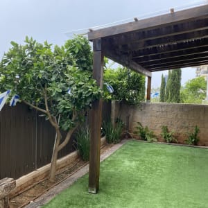 פרגולה מעץ בגינה עם דשא סינתטי ועצים