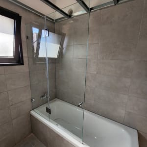 bathtub with glass shower screen and tiled walls