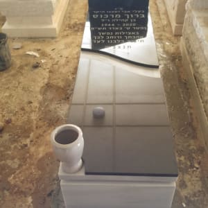 מצבה שחורה עם כיתוב בעברית על רקע אבן