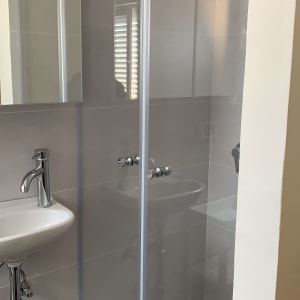 מקלחון זכוכית עם ברזים וכיור לידו