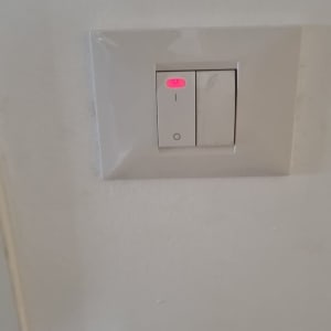 מתג חשמל כפול בקיר עם נורית חיווי אדומה דולקת