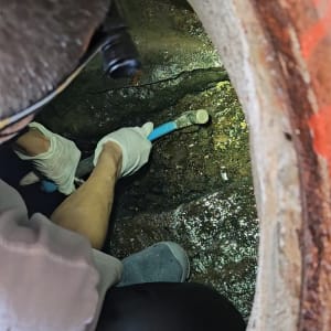 אדם עובד בצינור בתוך תעלה עם כפפות וכלי עבודה