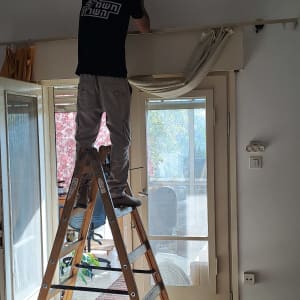 חשמלאי עומד על סולם ומתקן חוטים בתקרה