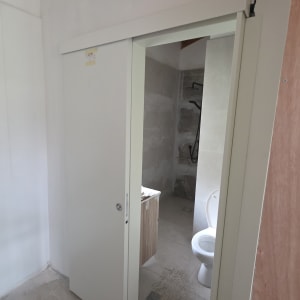 דלת הזזה לבנה בחדר אמבטיה עם שירותים ומקלחת