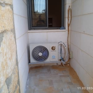 יחידת מיזוג אוויר מותקנת על קיר חיצוני ליד חלון.