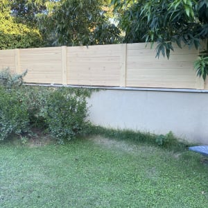 גדר עץ בהירה בגינה עם שיחים ועצים