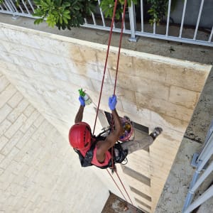 אדם עם קסדה אדומה עובד בגובה על קיר אבן