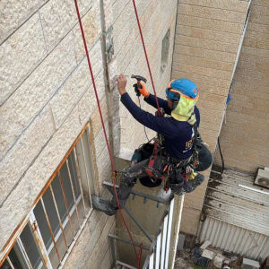 עובד בגובה עם קסדה וכלי עבודה על קיר בניין