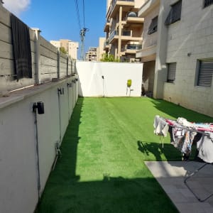 חצר עם דשא סינתטי וקיר עם צינור השקיה