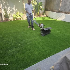 אדם עובד בגינה עם מכשיר גינון על דשא ירוק