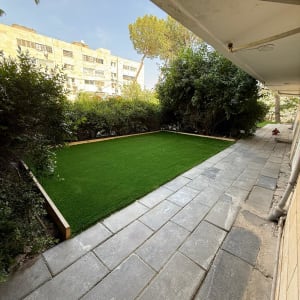 דשא סינתטי מוקף בשיחים, שביל מרוצף בצד