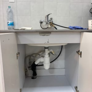 כיור עם ברז וצנרת מתחת לארון מטבח