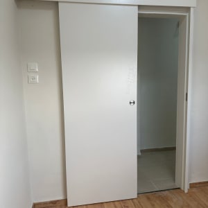 דלת הזזה לבנה עם ידית עגולה על רצפת עץ