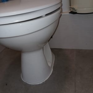 אסלה לבנה עם מכסה מעט פתוח על רצפת אריחים אפורה