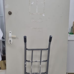 עגלת משא מתכתית עם ידיות שחורות על רקע דלת לבנה