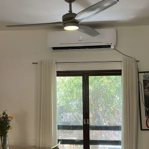 מזגן מותקן על קיר מעל חלון עם וילונות לבנים