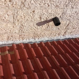 גג רעפים אדום עם קיר אבן וצינור קטן