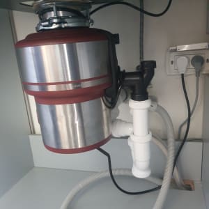 מכשיר טוחן אשפה מתחת לכיור עם צינורות חיבור