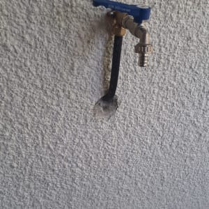 ברז עם ידית כחולה וצינור שחור בקיר