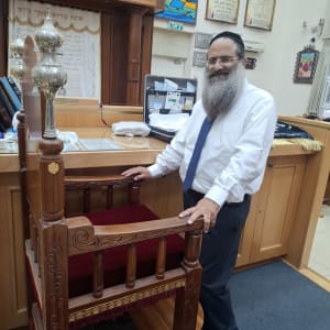 אדם עומד ליד כיסא בבית כנסת עם ספרי תורה
