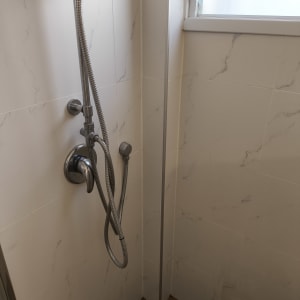 ראש מקלחת עם צינור מתכת על קיר אריחים