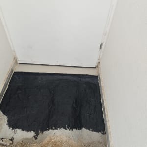 איטום רצפה עם חומר שחור ליד דלת לבנה